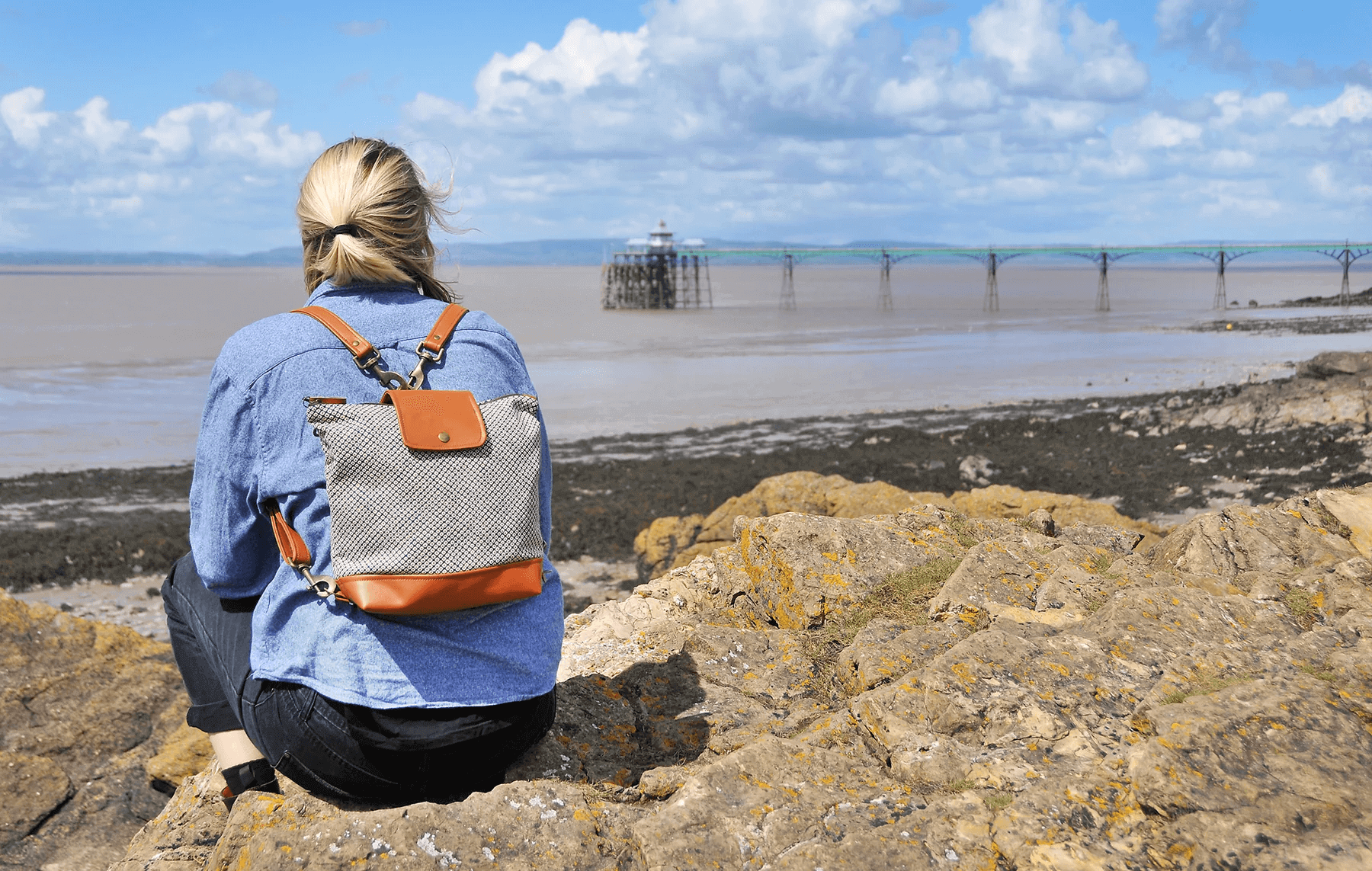 Woman wearing recycled leather convertible backpack at the beach. Handmade recycled leather handbags, backpack and accessories made from sustainable materials in Bristol, UK.