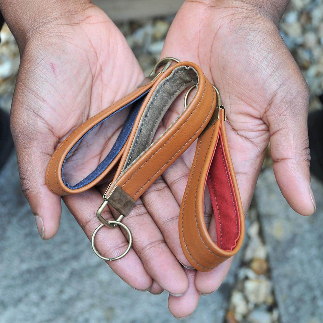 Hands holding recycled leather and wax canvas keychains
